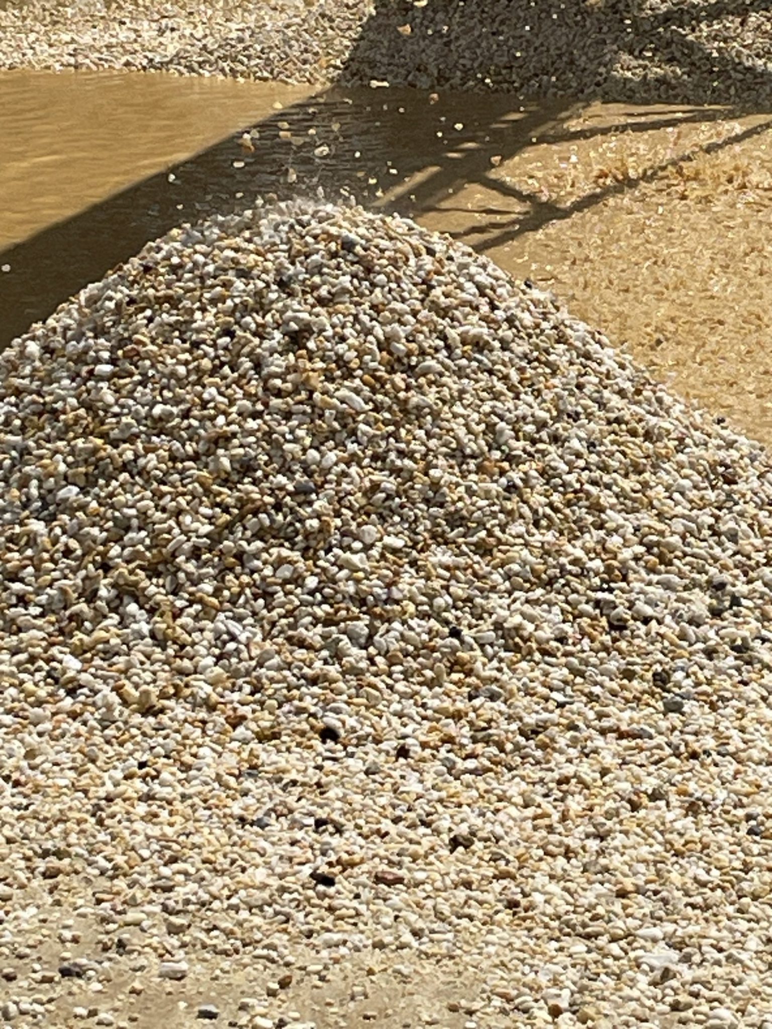 This image shows pea gravel being actively deposited, likely from a conveyor at a wash plant. The gravel is clean, rounded, and uniform in size, with a smooth texture ideal for decorative landscaping, drainage layers, or exposed aggregate concrete finishes.