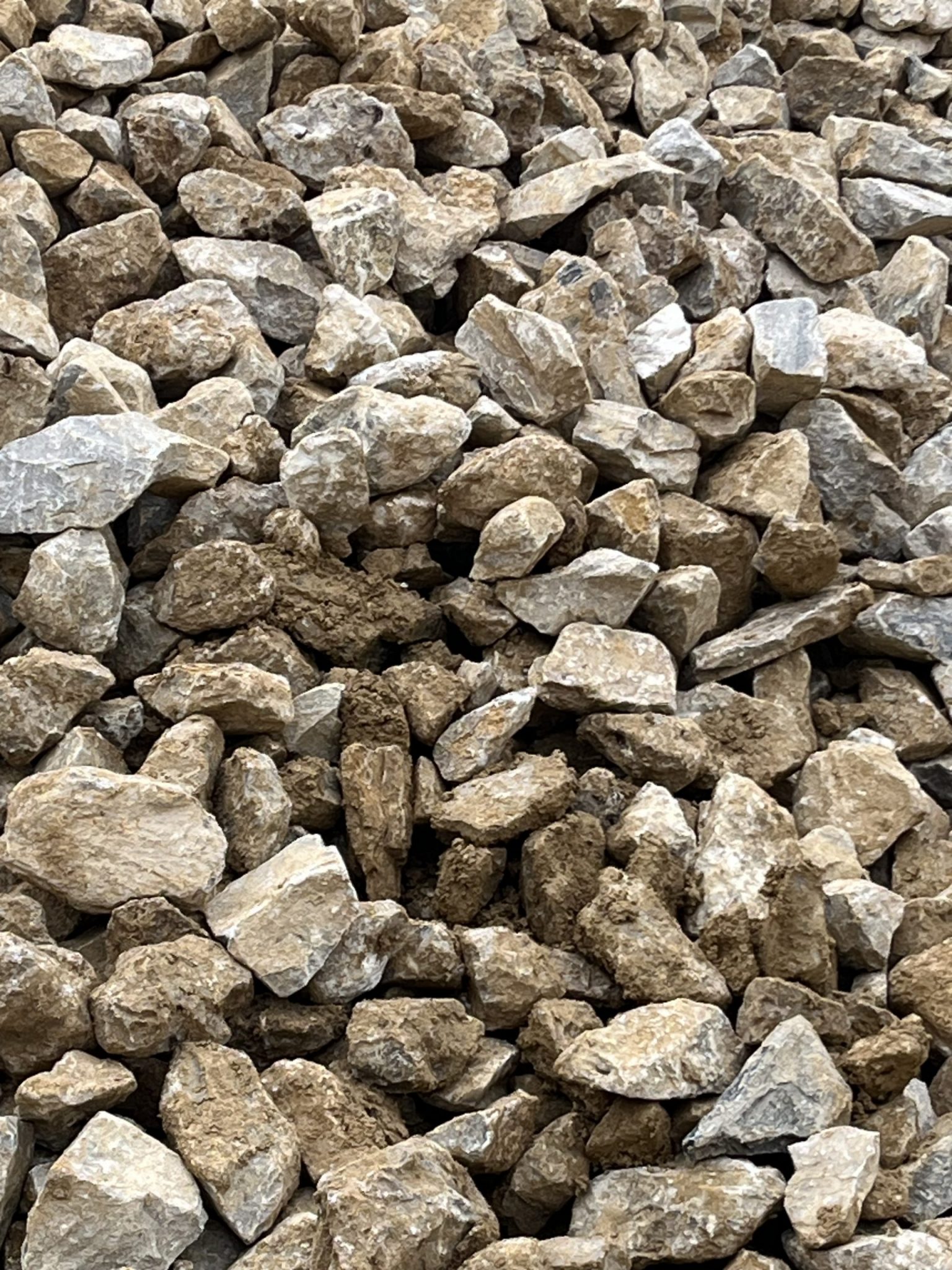 This pile of coarse aggregate displays a substantial amount of fine soil or clay coating the surfaces of the individual stones. Such contamination can significantly reduce the effectiveness of the aggregate in applications like concrete or drainage due to poor bonding and reduced permeability. Proper washing and quality control are essential before use.